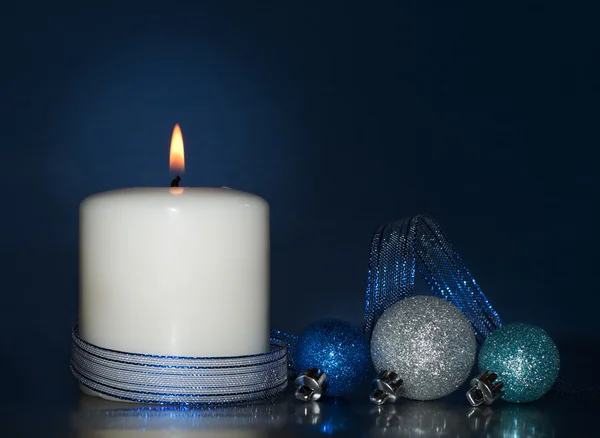 White Christmas candle burning, with glittering baubles on dark blue background — Stock Photo, Image