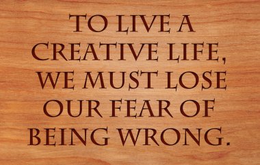 To live a creative life, we must lose our fear of being wrong - quote on wooden red oak background clipart