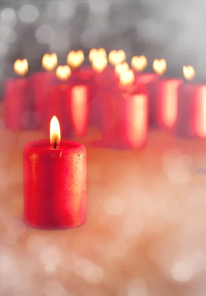 Imagem sonhadora de uma vela de Natal vermelha queimando, com velas semelhantes no fundo com corações para chamas — Fotografia de Stock