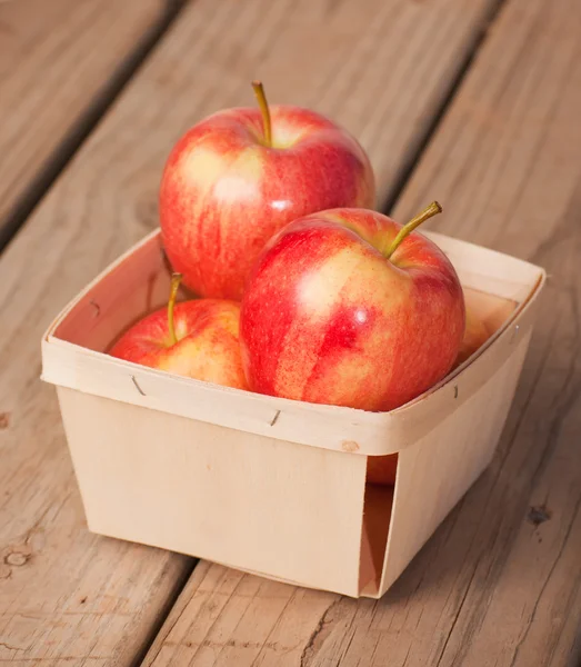 Rote und gelbe Äpfel in einem kleinen geflochtenen Holzkorb auf rustikalem Papphintergrund — Stockfoto