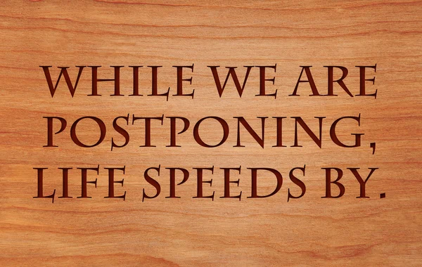 While we are postponing, life speeds by - quote on wooden red oak background — Stock Photo, Image