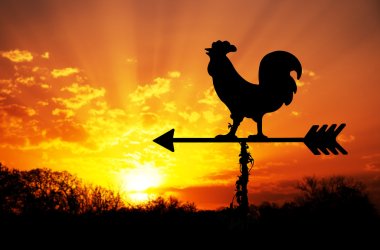 Rooster weathervane against sunrise with bright colors in clouds, concept for early morning wake up