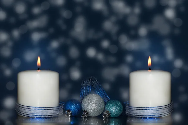 Dos velas blancas con una cinta azul y adornos navideños sobre un fondo onírico y nevado —  Fotos de Stock