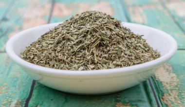 Ahşap arka plan üzerinde beyaz kase otlar tarhun kurutulmuş