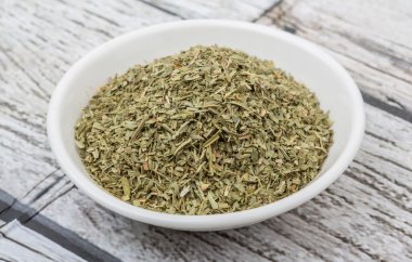 Ahşap arka plan üzerinde beyaz kase otlar tarhun kurutulmuş