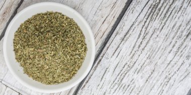 Ahşap arka plan üzerinde beyaz kase otlar tarhun kurutulmuş