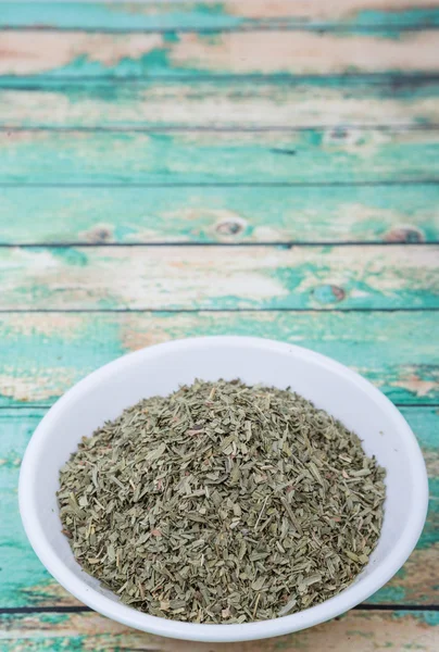 Dried tarragon herbs in white bowl over wooden background