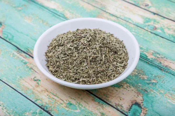 Dried tarragon herbs in white bowl over wooden background