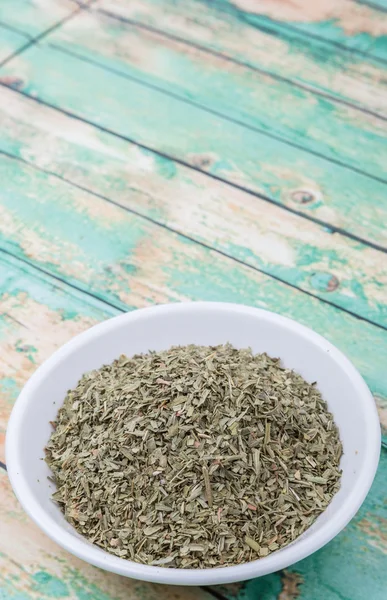 Dried tarragon herbs in white bowl over wooden background