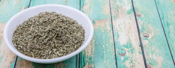 Dried tarragon herbs in white bowl over wooden background