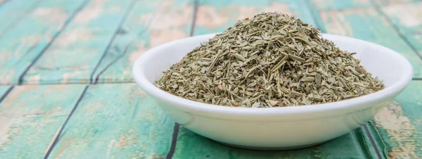 Dried tarragon herbs in white bowl over wooden background