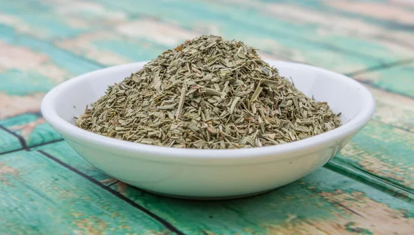 Dried tarragon herbs in white bowl over wooden background