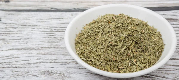 Dried tarragon herbs in white bowl over wooden background