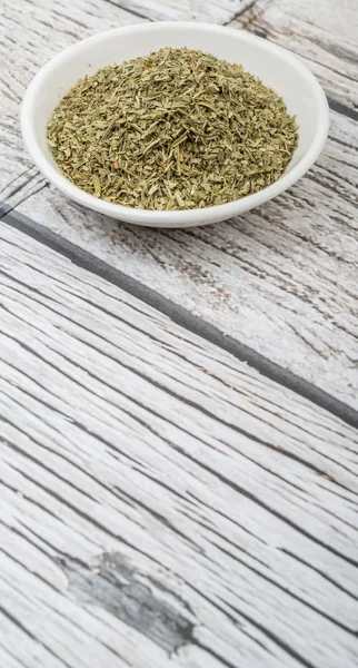 Dried tarragon herbs in white bowl over wooden background