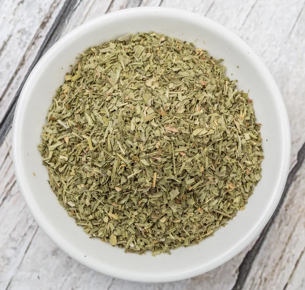 Dried tarragon herbs in white bowl over wooden background