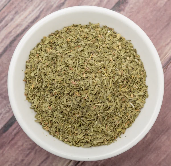 Dried tarragon herbs in white bowl over wooden background