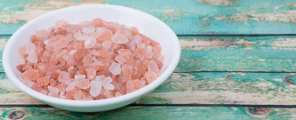 Himalayan rock salt in white bowl over wooden background