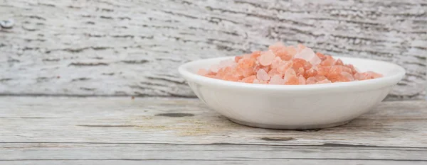 Himalayan rock salt in white bowl over wooden background