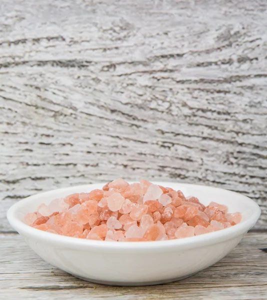 Himalayan rock salt in white bowl over wooden background