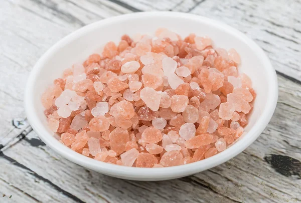 Himalayan rock salt in white bowl over wooden background