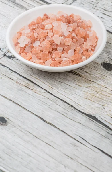 Himalayan rock salt in white bowl over wooden background