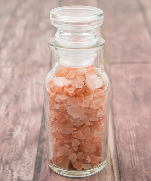 Himalayan rock salt in glass vial over wooden background