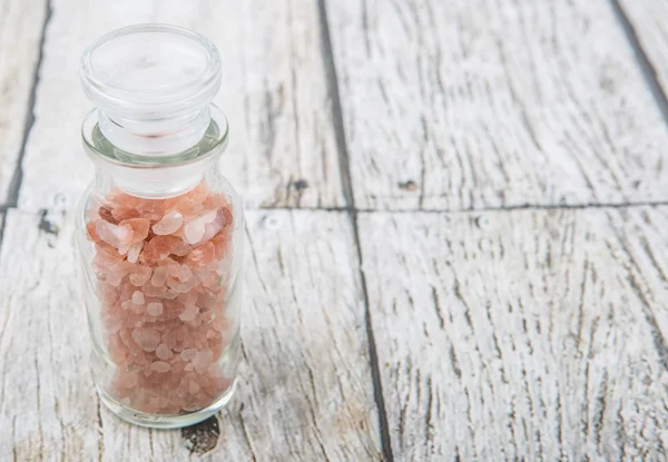 Himalayan rock salt in glass vial over wooden background