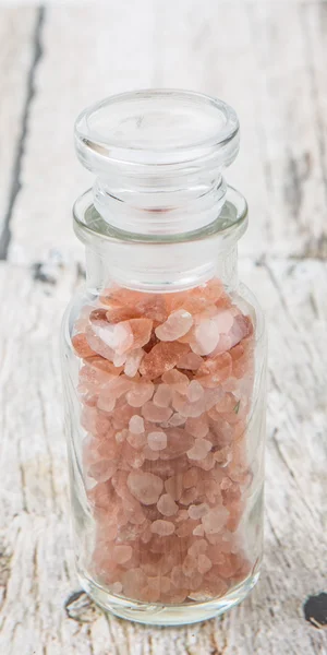 Himalayan rock salt in glass vial over wooden background