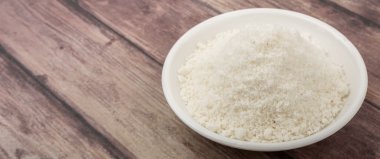 Ahşap zemin üzerinde beyaz kâsede kurutulmuş hindistan cevizi tozu.