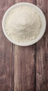 Ahşap zemin üzerinde beyaz kâsede kurutulmuş hindistan cevizi tozu.