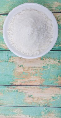 Ahşap zemin üzerinde beyaz kâsede kurutulmuş hindistan cevizi tozu.