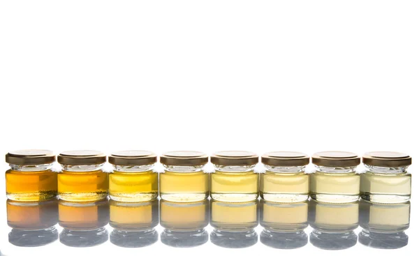 Different grades and colors of honey in mason jars over white background