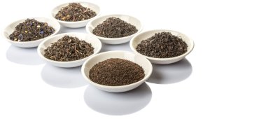 Beyaz arka plan üzerinde beyaz kase çeşitli gevşek ve kurutulmuş siyah çay yaprakları