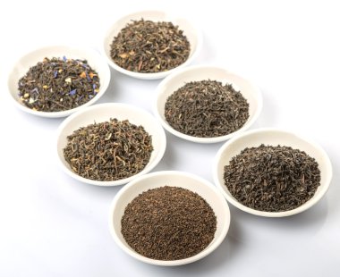 Beyaz arka plan üzerinde beyaz kase çeşitli gevşek ve kurutulmuş siyah çay yaprakları