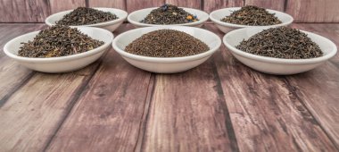 Ahşap arka plan üzerinde beyaz kase çeşitli gevşek ve kurutulmuş siyah çay yaprakları