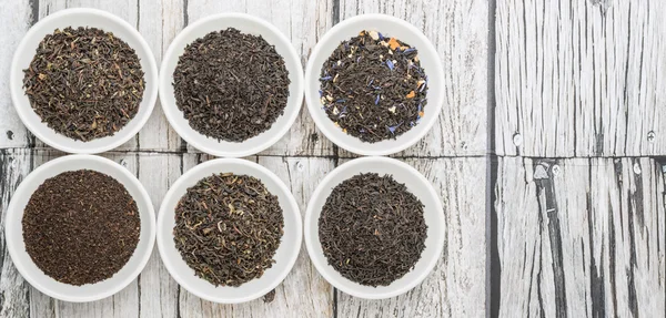 Loose and dried black tea leaves variety in white bowls over wooden background