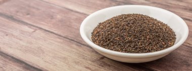 Ahşap arka plan üzerinde beyaz kase gevşek kurutulmuş darjeeling siyah çay yaprakları