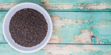 Ahşap arka plan üzerinde beyaz kase gevşek kurutulmuş darjeeling siyah çay yaprakları