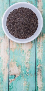 Ahşap arka plan üzerinde beyaz kase gevşek kurutulmuş darjeeling siyah çay yaprakları