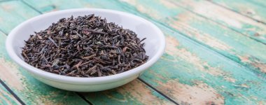 Ahşap arka plan üzerinde beyaz kase gevşek kurutulmuş darjeeling siyah çay yaprakları