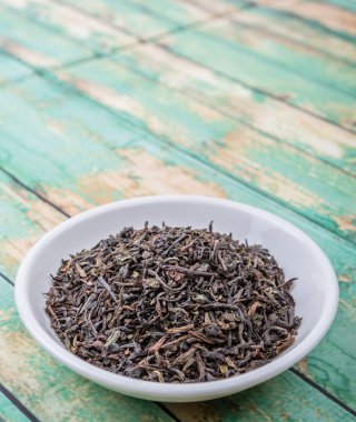 Ahşap arka plan üzerinde beyaz kase gevşek kurutulmuş darjeeling siyah çay yaprakları