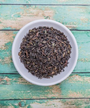 Ahşap arka plan üzerinde beyaz kase gevşek kurutulmuş darjeeling siyah çay yaprakları