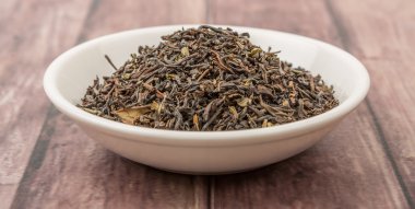 Ahşap arka plan üzerinde beyaz kase gevşek kurutulmuş darjeeling siyah çay yaprakları