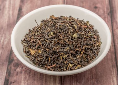 Ahşap arka plan üzerinde beyaz kase gevşek kurutulmuş darjeeling siyah çay yaprakları