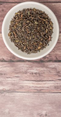 Ahşap arka plan üzerinde beyaz kase gevşek kurutulmuş darjeeling siyah çay yaprakları