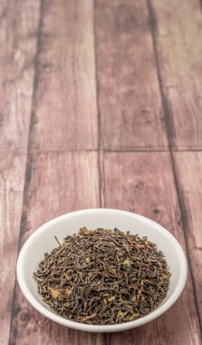 Ahşap arka plan üzerinde beyaz kase gevşek kurutulmuş darjeeling siyah çay yaprakları