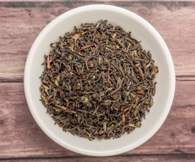 Ahşap arka plan üzerinde beyaz kase gevşek kurutulmuş darjeeling siyah çay yaprakları