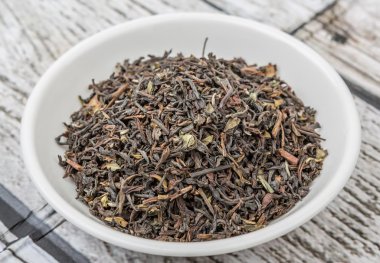 Ahşap arka plan üzerinde beyaz kase gevşek kurutulmuş darjeeling siyah çay yaprakları