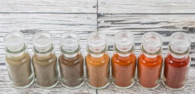 Soğuk toz, cayenne tozu, kırmızı biber tozu, karabiber toz, beyaz biber tozu, karabiber toz ahşap arka plan üzerinde cam şişe içinde ürün yelpazesine