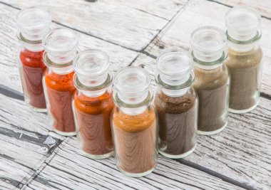 Soğuk toz, cayenne tozu, kırmızı biber tozu, karabiber toz, beyaz biber tozu, karabiber toz ahşap arka plan üzerinde cam şişe içinde ürün yelpazesine